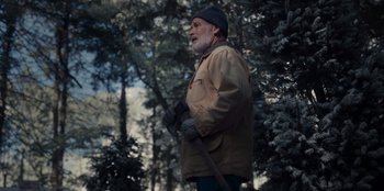 Movie still from “The Noel Diary” (2022), directed by Charles Shyer – An older man with a beard is standing in the woods; Medium shot, Low angle