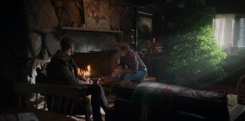 Movie still from “The Noel Diary” (2022), directed by Charles Shyer – Two men sitting in front of a fire in a living room; Wide shot, Over the shoulder angle