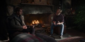 Movie still from “The Noel Diary” (2022), directed by Charles Shyer – Two men sitting in front of a fire place; Wide shot, Over the shoulder angle