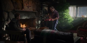 Movie still from “The Noel Diary” (2022), directed by Charles Shyer – A man standing in front of a fireplace holding something; Wide shot, Over the shoulder angle