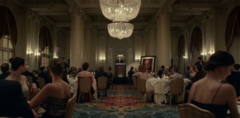 Movie still from “Dopesick” (2021), directed by Danny Strong – People are sitting at tables in an ornate room; Extreme Wide shot, Over the shoulder angle
