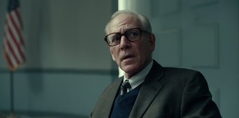 Movie still from “Dopesick” (2021), directed by Danny Strong – An older man wearing glasses and a suit; Close Up shot, Low angle