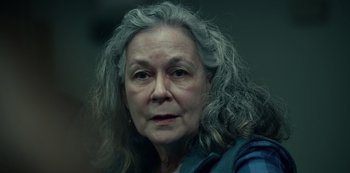 Movie still from “Dopesick” (2021), directed by Danny Strong – An older woman with long gray hair looking at the camera; Close Up shot, Over the shoulder angle