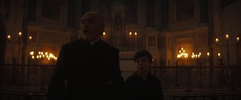 Movie still from “The Nun II” (2023), directed by Michael Chaves – A man and a boy standing next to each other in front of a building; Medium shot, Low angle