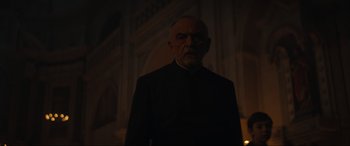Movie still from “The Nun II” (2023), directed by Michael Chaves – An older man in a black suit standing in front of a building; Medium shot, Low angle