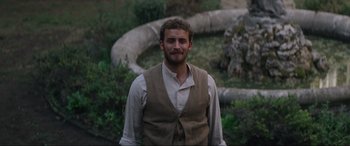 Movie still from “The Nun II” (2023), directed by Michael Chaves – A man wearing a vest standing in front of trees; Medium shot, Over the shoulder angle