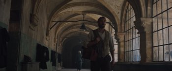 Movie still from “The Nun II” (2023), directed by Michael Chaves – A man with a beard holding a purse in a hallway; Wide shot, Low angle