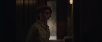 Movie still from “The Nun II” (2023), directed by Michael Chaves – A young man wearing a hat standing in front of a door; Medium shot, Over the shoulder angle
