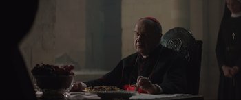 Movie still from “The Nun II” (2023), directed by Michael Chaves – An older man sitting at a table with a plate of food in front of him; Close Up shot, Over the shoulder angle
