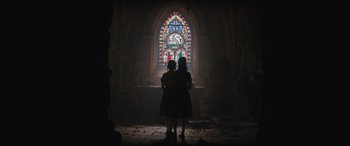 Movie still from “The Nun II” (2023), directed by Michael Chaves – Two people standing in front of a stained - glass window; Extreme Wide shot, Low angle