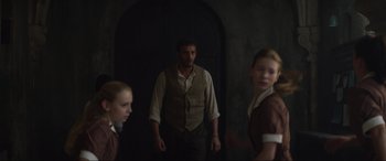 Movie still from “The Nun II” (2023), directed by Michael Chaves – A man and two girls standing in front of an archway; Medium shot, Over the shoulder angle