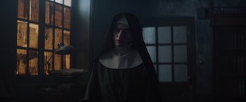 Movie still from “The Nun II” (2023), directed by Michael Chaves – A woman dressed as a nun standing in front of a window; Close Up shot, Low angle