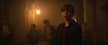 Movie still from “The Nun II” (2023), directed by Michael Chaves – A young man standing in a room with other people; Medium shot, Over the shoulder angle