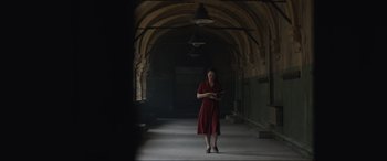 Movie still from “The Nun II” (2023), directed by Michael Chaves – A woman in a red dress standing in an archway holding a tablet; Wide shot, Low angle