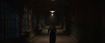 Movie still from “The Nun II” (2023), directed by Michael Chaves – A woman in a long black dress and a white headscarf is walking in a dark hallway; Wide shot, Low angle