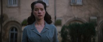 Movie still from “The Nun II” (2023), directed by Michael Chaves – A woman in a blue shirt is standing in front of a building; Close Up shot, Over the shoulder angle