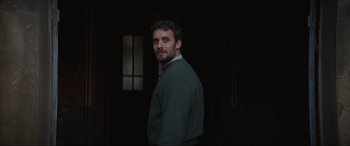 Movie still from “The Nun II” (2023), directed by Michael Chaves – A man standing in a dark room wearing a green sweater; Medium shot, Over the shoulder angle