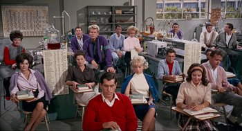 Movie still from “The Nutty Professor” (1963), directed by Jerry Lewis – A group of people sitting in a room with books on their laps; Wide shot, High angle