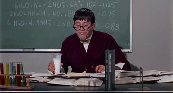 Movie still from “The Nutty Professor” (1963), directed by Jerry Lewis – A man sitting at a table with a glass of milk and a book; Medium shot, High angle