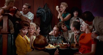 Movie still from “The Nutty Professor” (1963), directed by Jerry Lewis – A group of people sitting at a table with plates of food; Medium shot, High angle