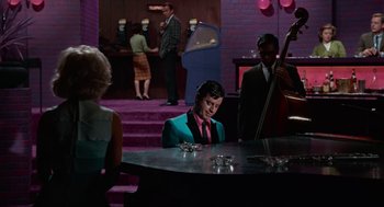 Movie still from “The Nutty Professor” (1963), directed by Jerry Lewis – A woman sitting at a table in front of a piano; Wide shot, Over the shoulder angle