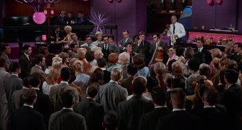 Movie still from “The Nutty Professor” (1963), directed by Jerry Lewis – A group of people sitting in front of each other on a stage; Extreme Wide shot, High angle