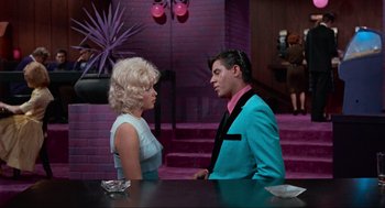 Movie still from “The Nutty Professor” (1963), directed by Jerry Lewis – A man and a woman are talking to each other in front of a purple wall; Medium shot, Low angle