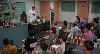 Movie still from “The Nutty Professor” (1963), directed by Jerry Lewis – A group of people sitting in front of a man in a kitchen; Wide shot, High angle