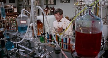 Movie still from “The Nutty Professor” (1963), directed by Jerry Lewis – A man in a white lab coat is working in a lab; Medium shot, High angle