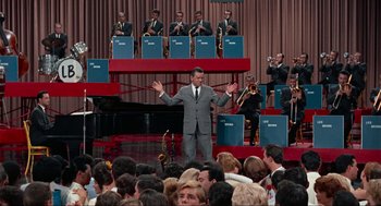 Movie still from “The Nutty Professor” (1963), directed by Jerry Lewis – A man in a gray suit is standing in front of a group of people; Wide shot, High angle