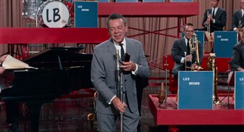 Movie still from “The Nutty Professor” (1963), directed by Jerry Lewis – A man holding a microphone while standing in front of an audience; Medium shot, High angle