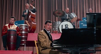 Movie still from “The Nutty Professor” (1963), directed by Jerry Lewis – A man sitting at a piano in front of a band; Medium shot, High angle