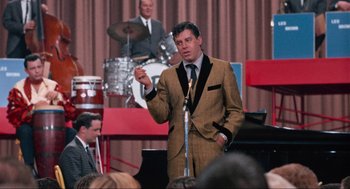 Movie still from “The Nutty Professor” (1963), directed by Jerry Lewis – A man wearing a suit and tie standing in front of a microphone; Medium shot, Low angle