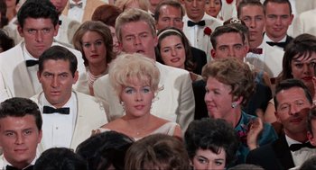 Movie still from “The Nutty Professor” (1963), directed by Jerry Lewis – A crowd of people in white suits and tuxedos; Medium shot, Low angle