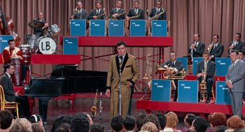 Movie still from “The Nutty Professor” (1963), directed by Jerry Lewis – A man in a brown suit standing in front of a group of people; Wide shot, High angle