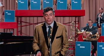 Movie still from “The Nutty Professor” (1963), directed by Jerry Lewis – A man wearing a suit and tie standing in front of a microphone; Medium shot, High angle