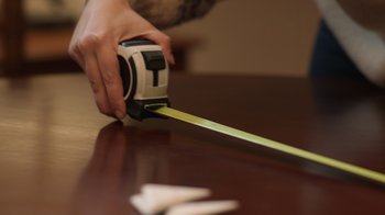 Movie still from “The Other Zoey” (2023), directed by Sara Zandieh – A person using a tape measure on a wooden table; Extreme Close Up shot, Low angle