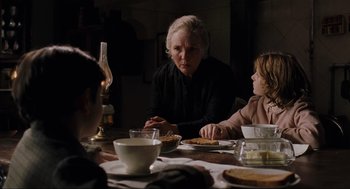 Movie still from “The Others” (2001), directed by Alejandro Amenábar – An older woman sitting at a dinner table with two children; Medium shot, Over the shoulder angle