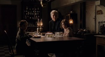 Movie still from “The Others” (2001), directed by Alejandro Amenábar – A group of people sitting at a table with a cake on it; Medium shot, Over the shoulder angle