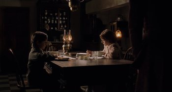 Movie still from “The Others” (2001), directed by Alejandro Amenábar – Two people sitting at a table in a dark room; Medium shot, High angle