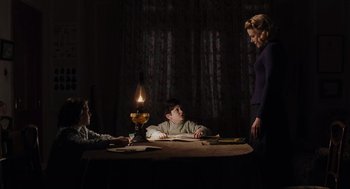 Movie still from “The Others” (2001), directed by Alejandro Amenábar – Three people sitting at a table in a dimly - lit room; Medium shot, Over the shoulder angle