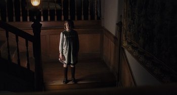 Movie still from “The Others” (2001), directed by Alejandro Amenábar – A little girl standing in a dark room holding a bag; Wide shot, High angle