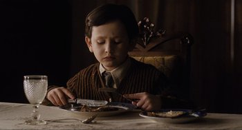 Movie still from “The Others” (2001), directed by Alejandro Amenábar – A young boy sitting at a table with a knife and fork in front of him; Medium shot, High angle