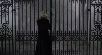 Movie still from “The Others” (2001), directed by Alejandro Amenábar – A woman in a long black coat standing in front of an iron gate; Wide shot, Over the shoulder angle