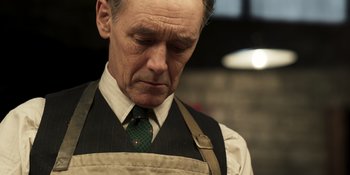 Movie still from “The Outfit” (2022), directed by Graham Moore – An older man wearing an apron looking down; Close Up shot, Low angle