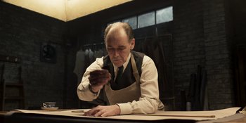 Movie still from “The Outfit” (2022), directed by Graham Moore – A man in an apron is working at a table; Medium shot, Low angle