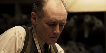 Movie still from “The Outfit” (2022), directed by Graham Moore – An older man with a measuring tape around his neck; Close Up shot, Low angle