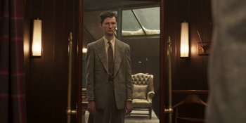 Movie still from “The Outfit” (2022), directed by Graham Moore – A man in a suit standing in front of an open door; Medium shot, Low angle