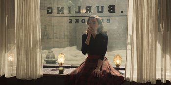 Movie still from “The Outfit” (2022), directed by Graham Moore – A woman sitting in front of a store window smoking a cigarette; Medium shot, High angle