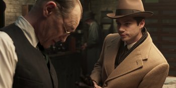 Movie still from “The Outfit” (2022), directed by Graham Moore – A man in a suit and a hat looking at another man in a hat; Medium shot, Over the shoulder angle